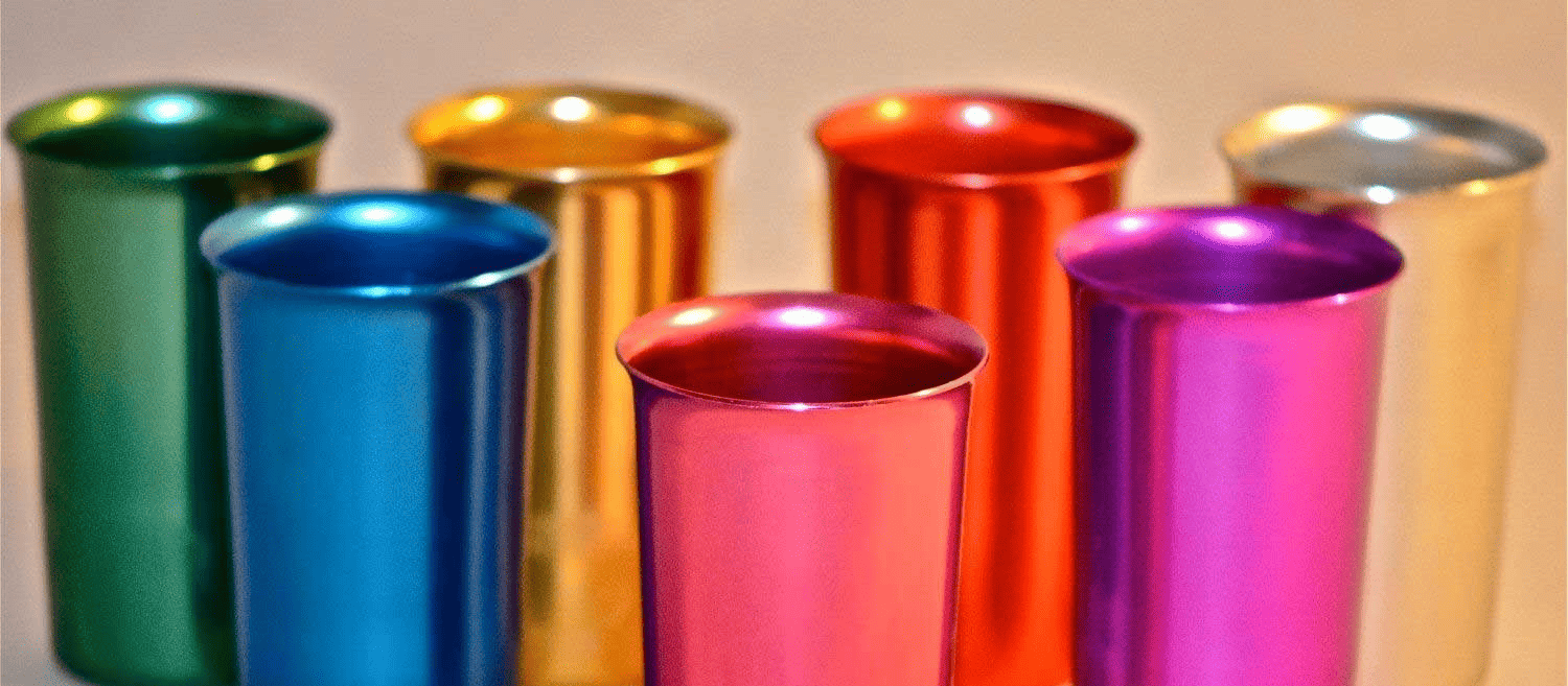 Metallic cups in green, blue, gold, red, purple, and pink colors, arranged on a light surface, with a shiny finish.