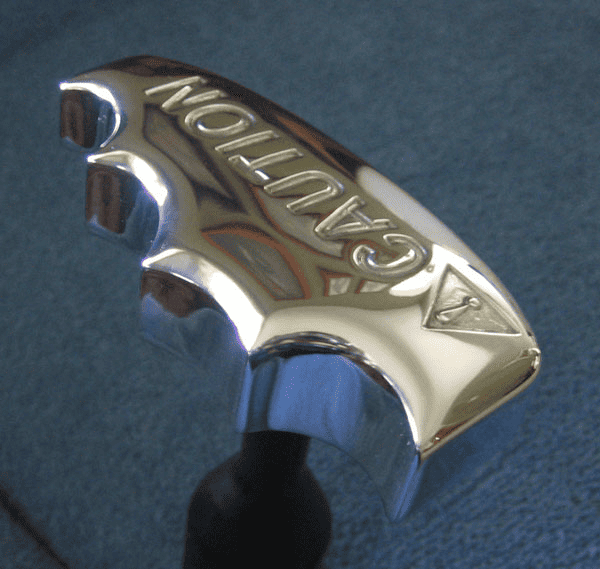 A shiny metal sign with a curved shape and "CAUTION" embossed text, featuring a black cord.