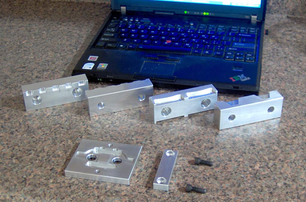 Silver metal parts and black screws on a granite countertop with an open blue laptop.