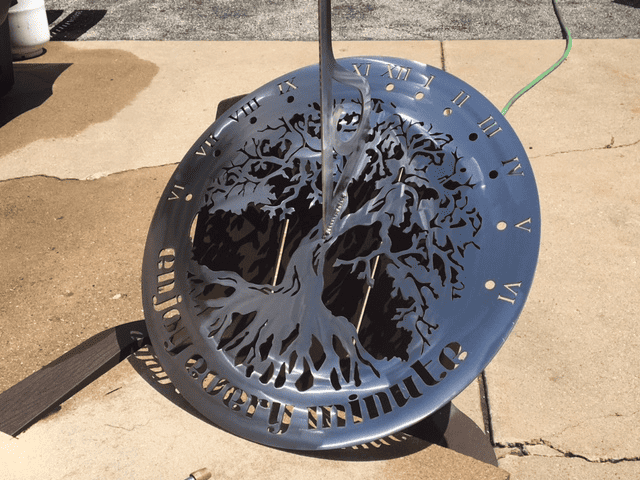 Decorative sundial with intricate design featuring tree and gold lettering on dark blue background.