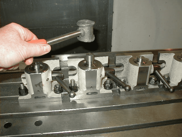 A hand holds a hammer over a metal workbench with an object attached.