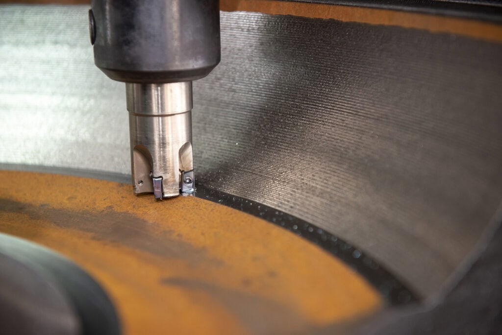 Close-up view of a cylindrical metal fabrication tool with silver cutting edge and black handle resting on a piece of yellowish-brown metal.
