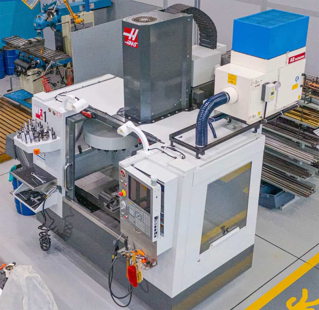 Industrial machine in a workshop with various components, including large white box and smaller boxes/tubes.